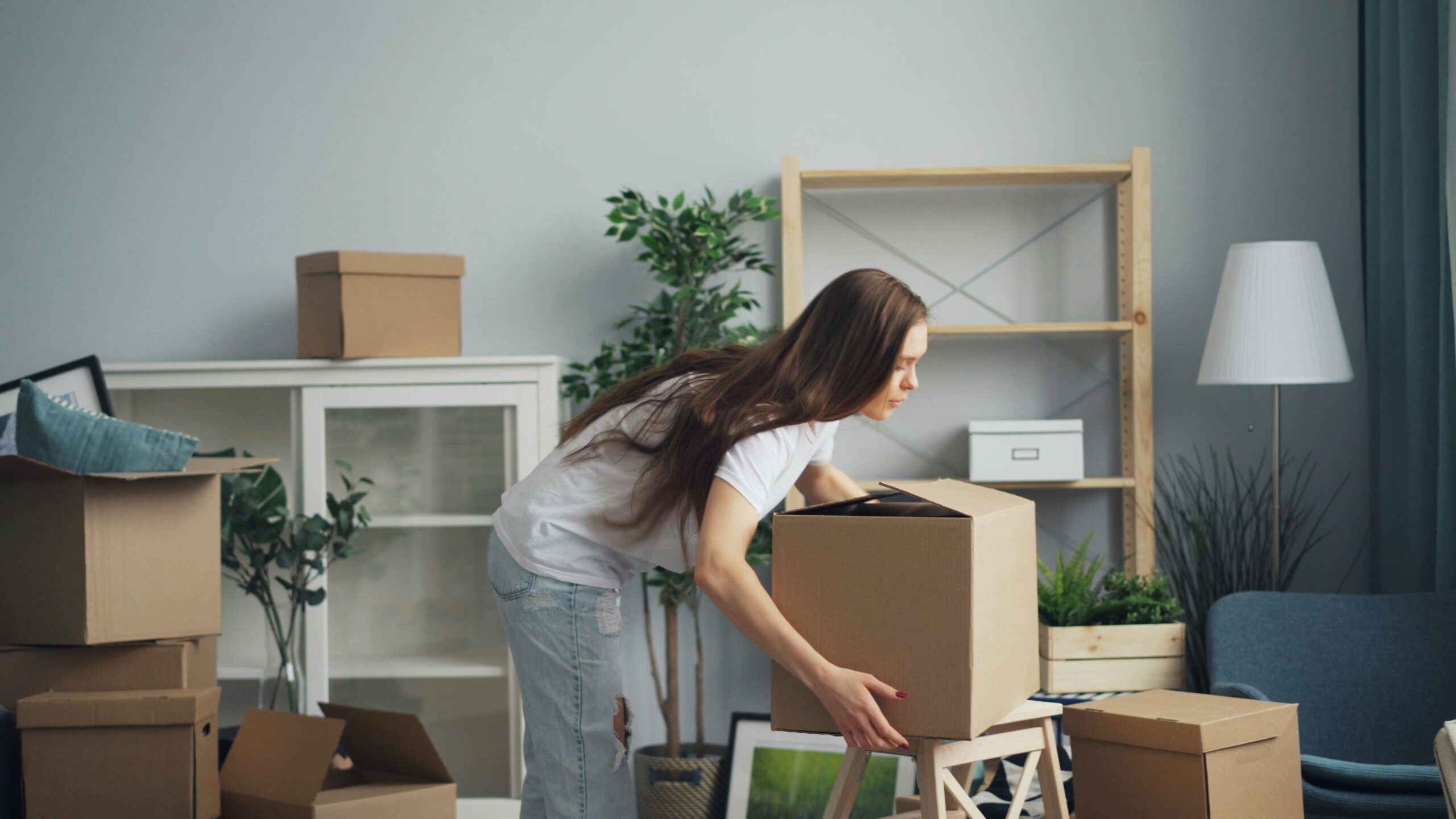 Woman lifting cardboard box to move out of apartment.